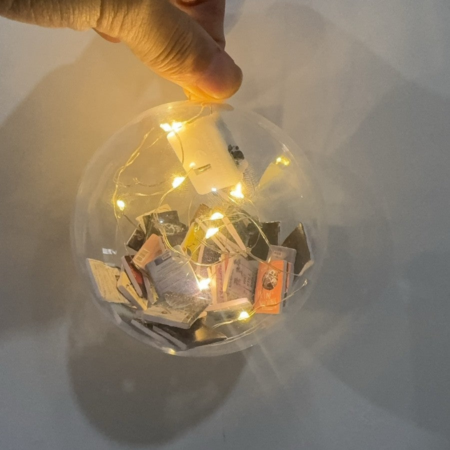 Hand holding a clear book-filled bauble