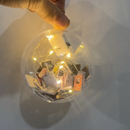 Hand holding a clear book-filled bauble